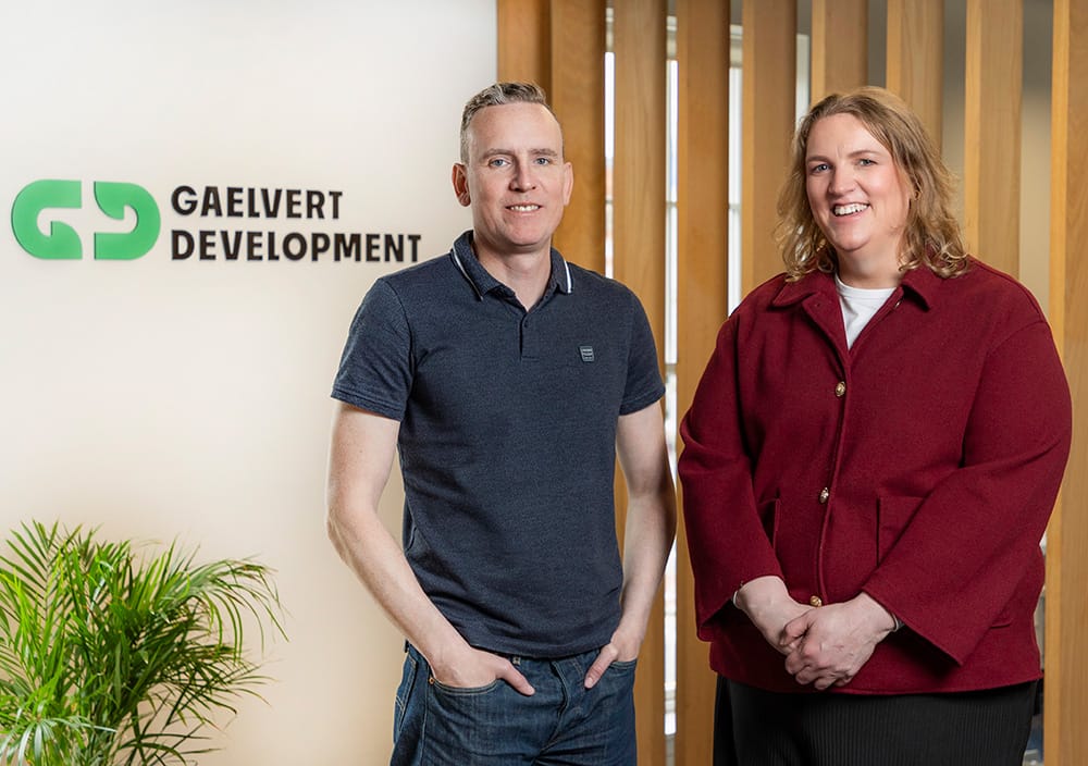 Man and woman standing together smiling in front of the Gaelvert Development logo wall
