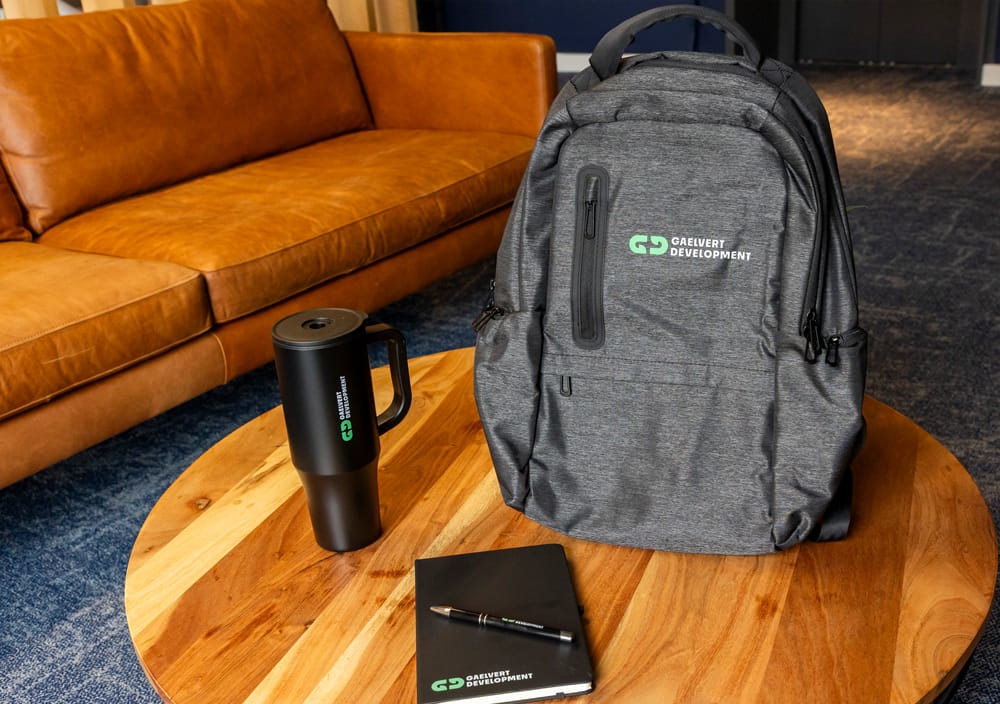 Branded Gaelvert Development merchandise: backpack, travel mug, notebook, and pen on a table