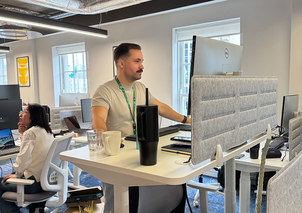 Colleague working at a standing desk in an open-plan office with monitors and privacy screens